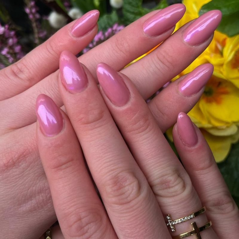Rosa Almond-Nägel mit perlmuttigem Schimmer vor Blumen